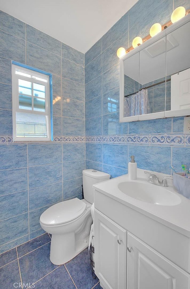 bathroom with toilet, a shower with curtain, tile patterned flooring, vanity, and tile walls