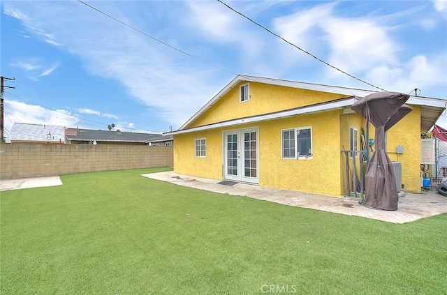 rear view of property featuring french doors, a lawn, fence, and stucco siding