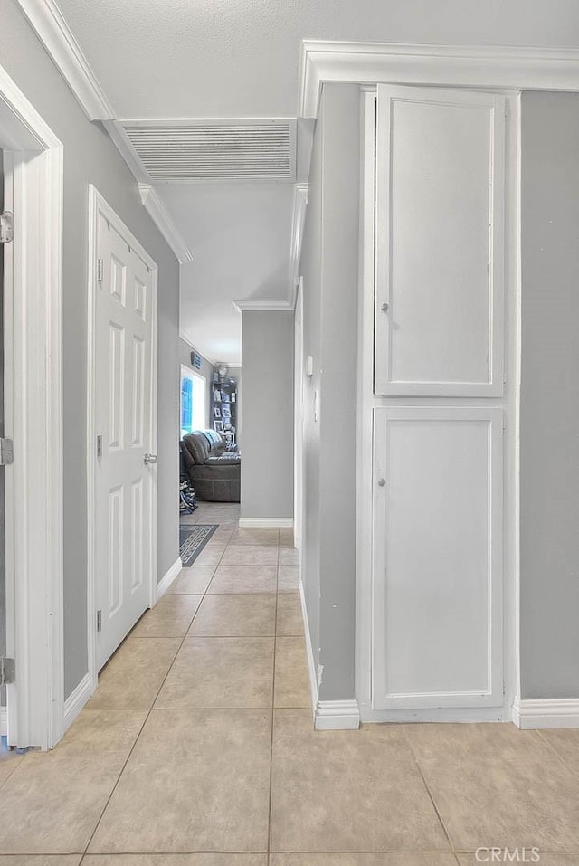 corridor featuring ornamental molding, light tile patterned flooring, visible vents, and baseboards