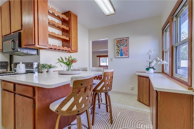 kitchen featuring black microwave, electric stove, light countertops, brown cabinets, and a kitchen bar