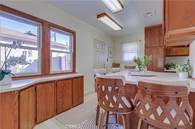 kitchen featuring visible vents, light countertops, a wealth of natural light, and brown cabinets