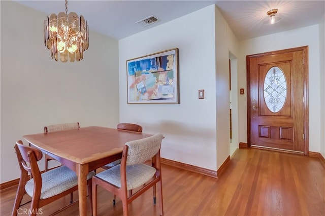 dining space featuring baseboards, visible vents, a chandelier, and wood finished floors