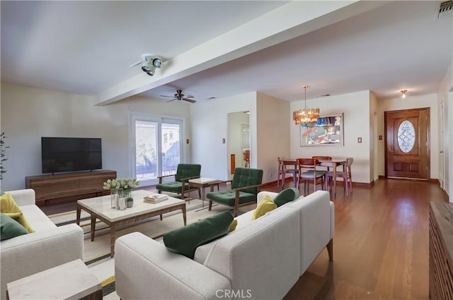 living area with ceiling fan with notable chandelier, beamed ceiling, wood finished floors, and visible vents