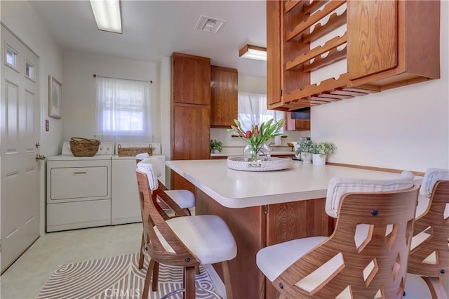 kitchen featuring visible vents, brown cabinets, light countertops, washer and dryer, and a wealth of natural light