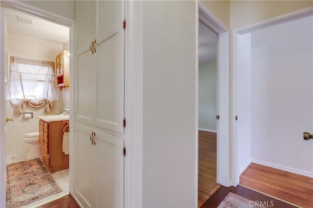 corridor featuring visible vents, light wood-style flooring, and baseboards