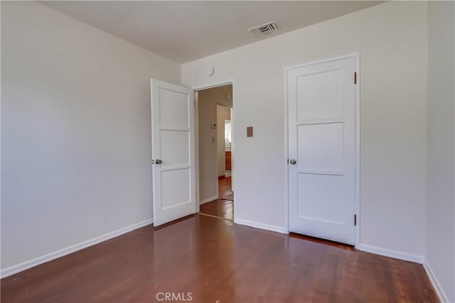 unfurnished room featuring baseboards, visible vents, and wood finished floors