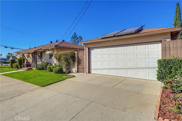 single story home with a garage, fence, roof mounted solar panels, a front lawn, and stucco siding