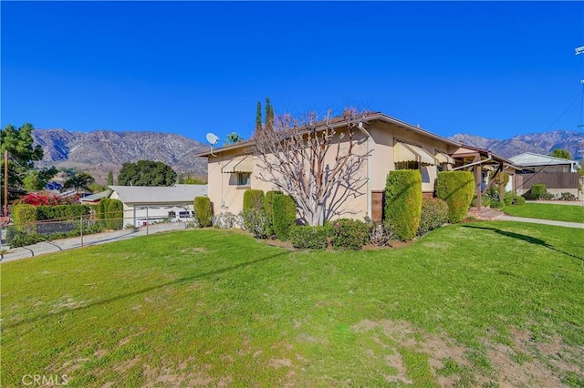 view of home's exterior with a mountain view, stucco siding, a lawn, and fence