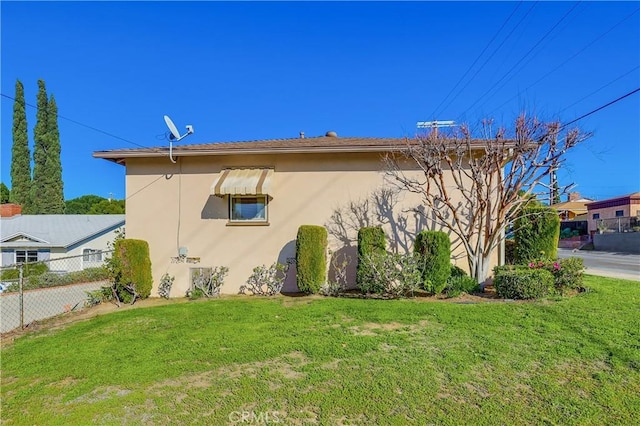 view of side of property with a lawn, fence, and stucco siding