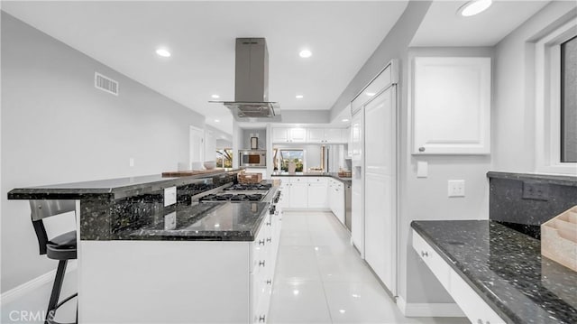 kitchen with visible vents, island exhaust hood, stainless steel microwave, dark stone counters, and white cabinets