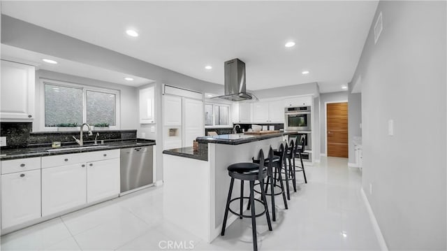 kitchen with a sink, island exhaust hood, a kitchen breakfast bar, stainless steel appliances, and white cabinets