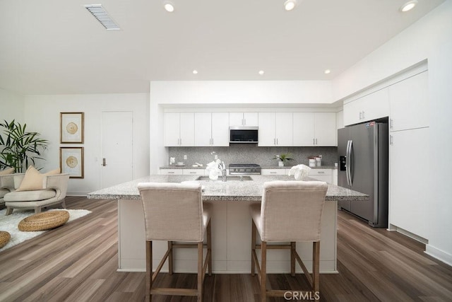 kitchen featuring visible vents, a kitchen breakfast bar, white cabinets, appliances with stainless steel finishes, and decorative backsplash