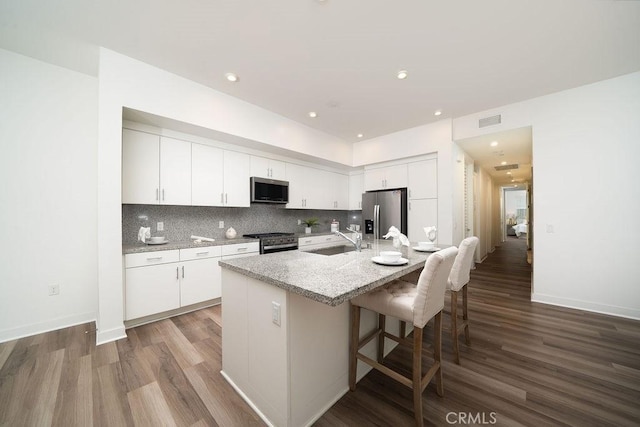 kitchen with stainless steel appliances, a sink, white cabinetry, tasteful backsplash, and a kitchen bar