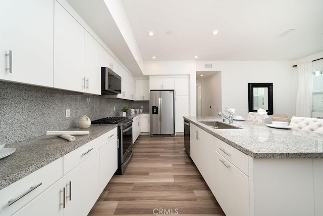 kitchen with stainless steel appliances, a sink, white cabinets, decorative backsplash, and light wood finished floors