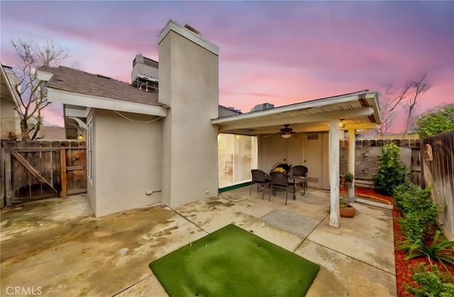 back of property with a patio, a fenced backyard, a ceiling fan, stucco siding, and a chimney