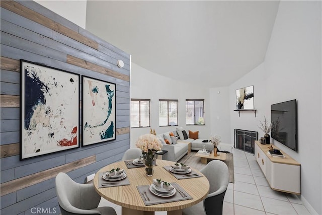 dining room featuring light tile patterned floors, high vaulted ceiling, and a glass covered fireplace