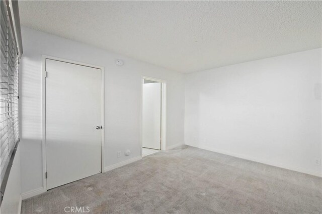 unfurnished bedroom with carpet flooring, a textured ceiling, and baseboards