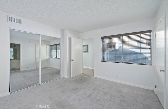 unfurnished bedroom featuring baseboards, visible vents, a textured ceiling, carpet floors, and a closet