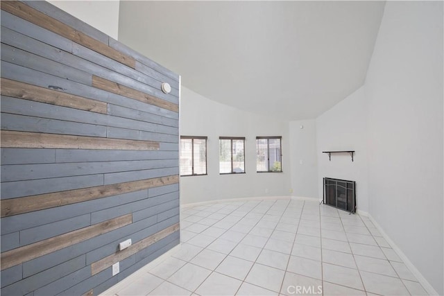 unfurnished living room with lofted ceiling, wooden walls, a fireplace, baseboards, and tile patterned floors