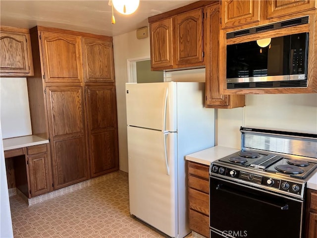 kitchen with brown cabinets, light countertops, stainless steel microwave, freestanding refrigerator, and black / electric stove