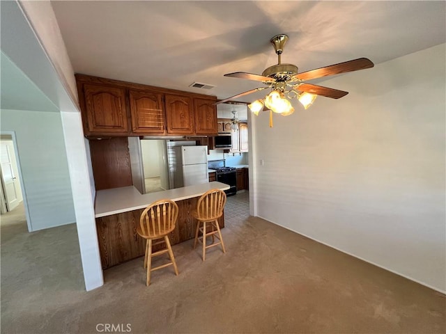 kitchen with a peninsula, visible vents, black gas stove, a kitchen breakfast bar, and freestanding refrigerator