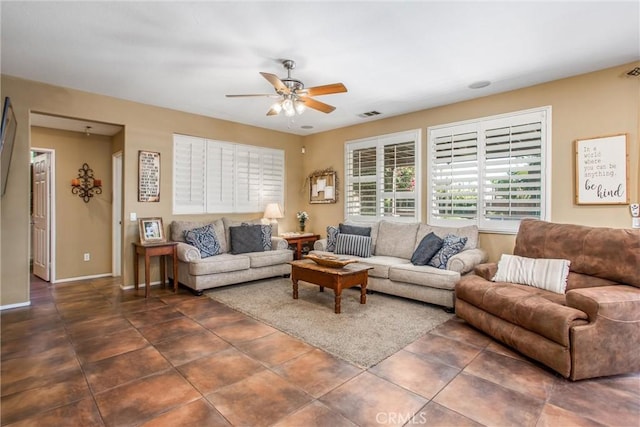 living area with a ceiling fan, visible vents, dark tile patterned floors, and baseboards