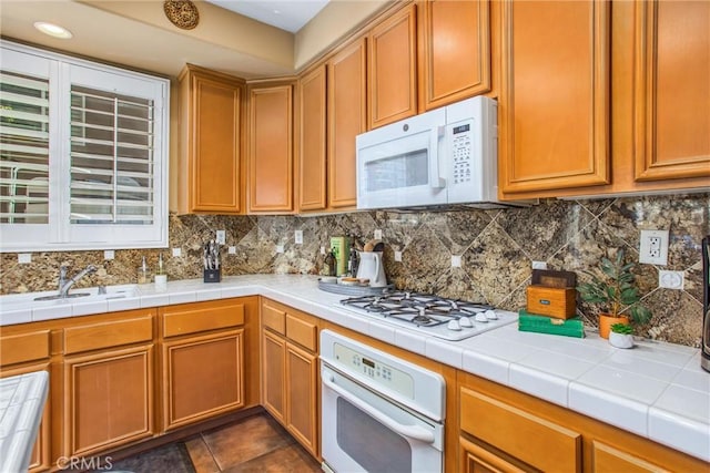 kitchen with dark tile patterned flooring, white appliances, a sink, and decorative backsplash