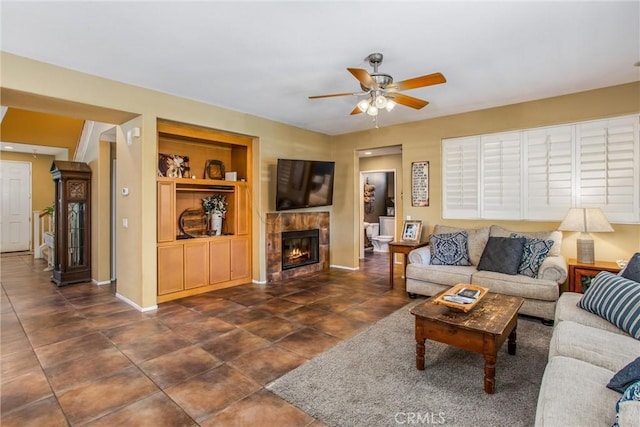 living area featuring built in shelves, dark tile patterned flooring, a fireplace, a ceiling fan, and baseboards