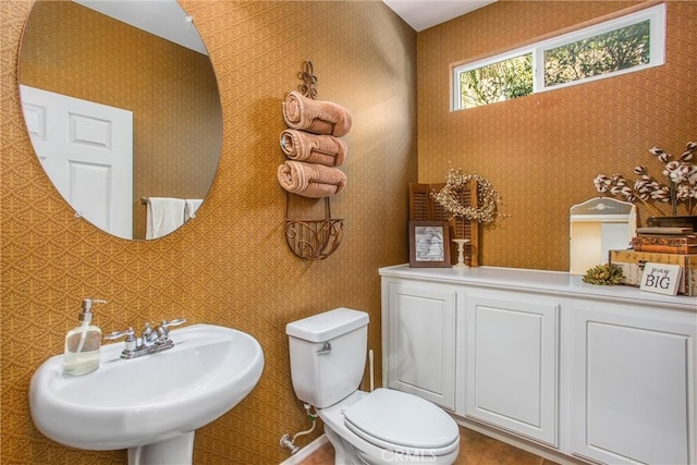 half bathroom with a sink, toilet, and wallpapered walls