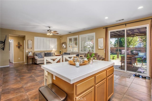 kitchen with tile countertops, ceiling fan, recessed lighting, visible vents, and a center island