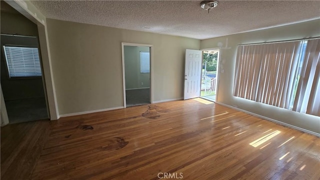 unfurnished room featuring a textured ceiling, baseboards, and wood finished floors