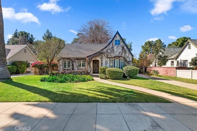 tudor home featuring stone siding, a front yard, and fence