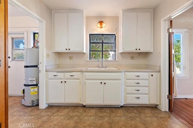 kitchen with white cabinets, water heater, light countertops, and a sink