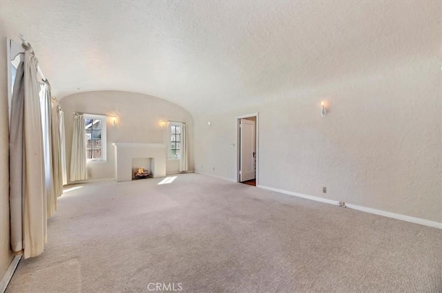 unfurnished living room featuring lofted ceiling, a warm lit fireplace, baseboards, and a textured ceiling