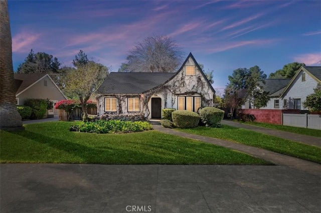 tudor-style house featuring a front yard, stone siding, and fence