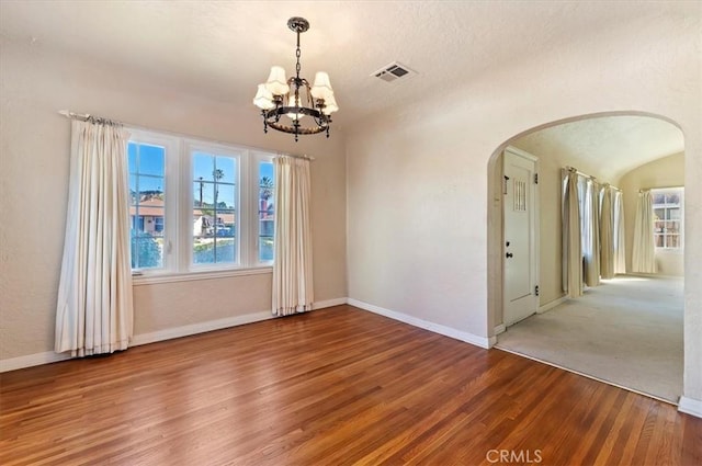 spare room featuring baseboards, visible vents, arched walkways, and wood finished floors