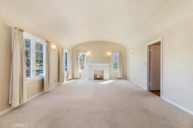 unfurnished living room with a fireplace with flush hearth, a wealth of natural light, a textured ceiling, and baseboards