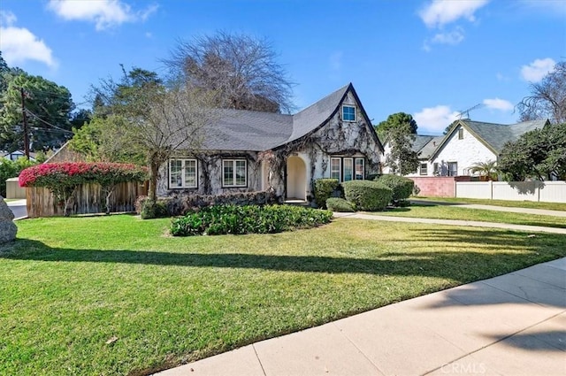 tudor house with stone siding, fence, and a front lawn