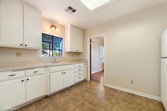 kitchen featuring baseboards, white cabinets, visible vents, light countertops, and a sink