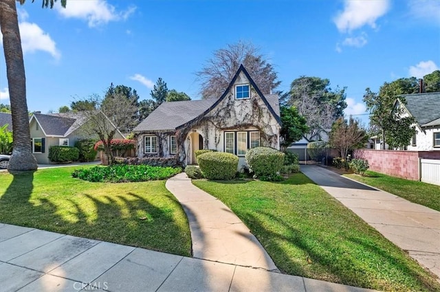 english style home with stone siding, fence, and a front lawn