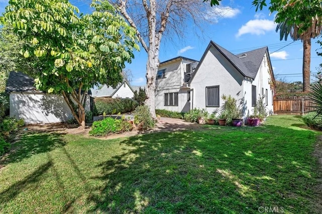 rear view of house with fence, a lawn, and stucco siding