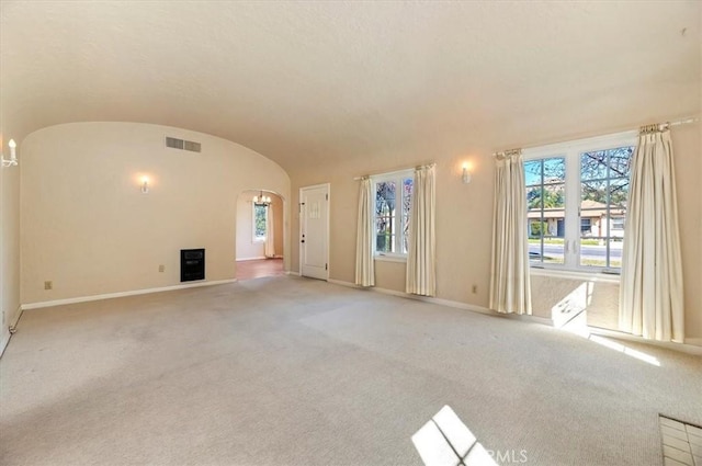 unfurnished living room with arched walkways, visible vents, light carpet, vaulted ceiling, and baseboards