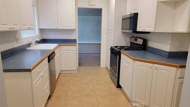 kitchen with appliances with stainless steel finishes, dark countertops, white cabinets, and a sink