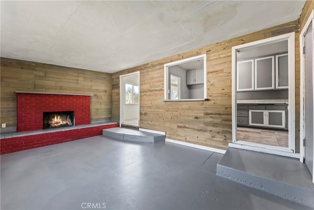 unfurnished living room featuring finished concrete flooring, wood walls, a fireplace, and baseboards