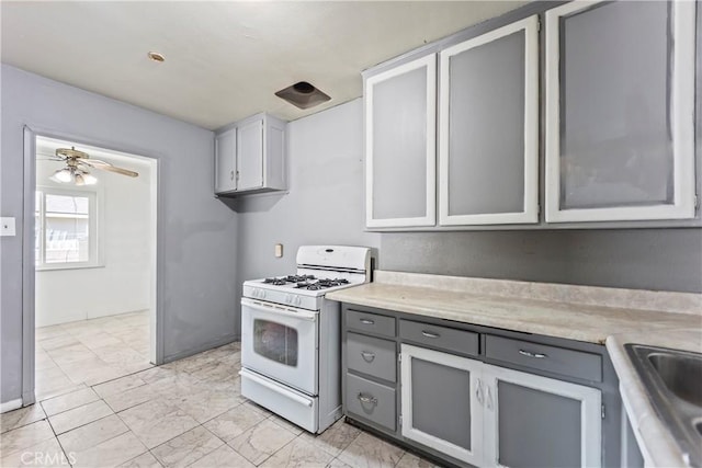 kitchen with a ceiling fan, gas range gas stove, light countertops, gray cabinetry, and a sink