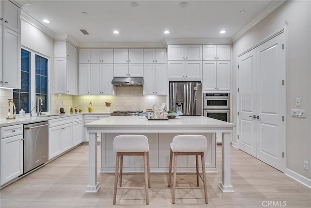 kitchen with under cabinet range hood, a breakfast bar, a sink, white cabinets, and appliances with stainless steel finishes