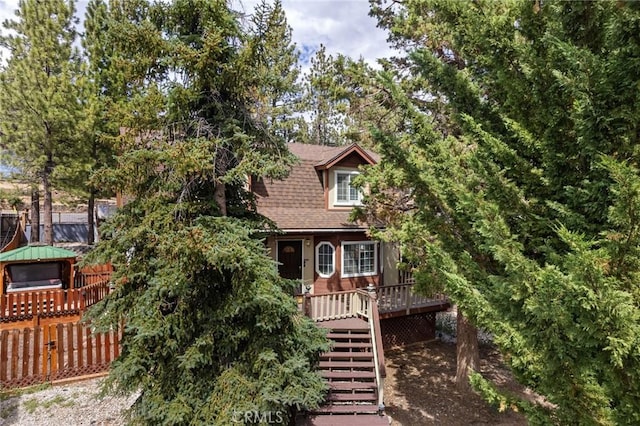 view of front of home with a shingled roof, fence, and stairway