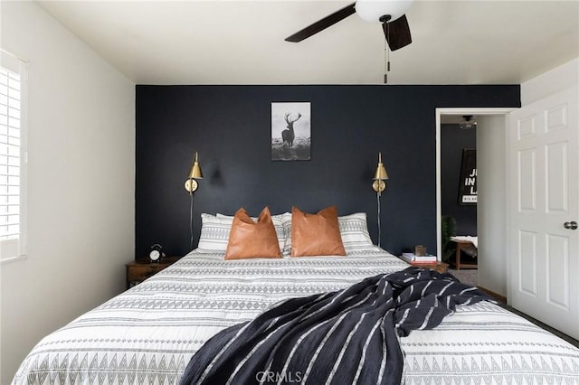 bedroom with an accent wall, multiple windows, a ceiling fan, and baseboards