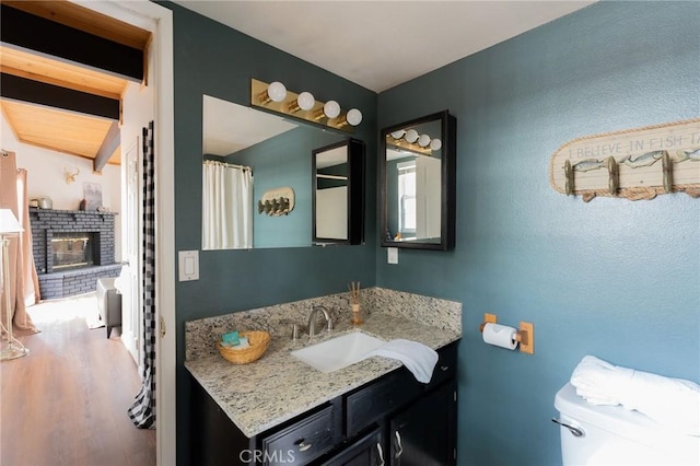 full bath with toilet, a fireplace, wood finished floors, and vanity