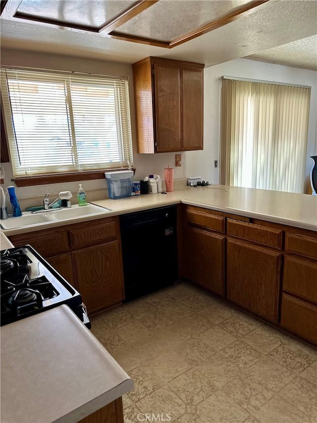 kitchen featuring range with gas cooktop, light countertops, brown cabinetry, a sink, and dishwasher